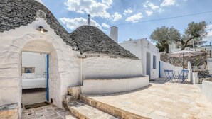 A traditional stone house with a white exterior, a stone staircase leading to a door, and a small outdoor seating area with a table and chairs. - Villa 'Borgo Trulli 1817' with Private Pool, Wi-Fi and Air Conditioning (Putignano)
