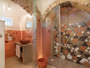 Une salle de bain avec une arche en pierre, une douche fermée par des parois de verre, un lavabo en forme de vasque et un mur orné d’un motif.
