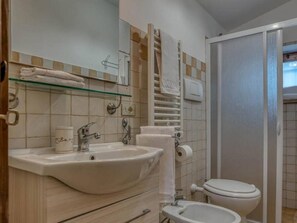 A bathroom with a sink, bidet, toilet, and a glass shelf with towels.