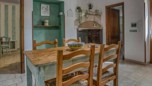 Un comedor con mesa y sillas de madera, una pared verde con un cuadro, y una zona de cocina con estufa y armarios.