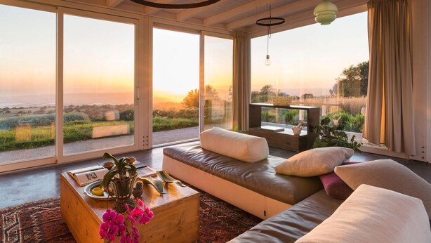 A spacious living room with a large window offering a view of the countryside. There is a sofa with cushions, a coffee table with decorative items, and a small TV on a stand. - Amazing home in Ragusa (Ragusa)