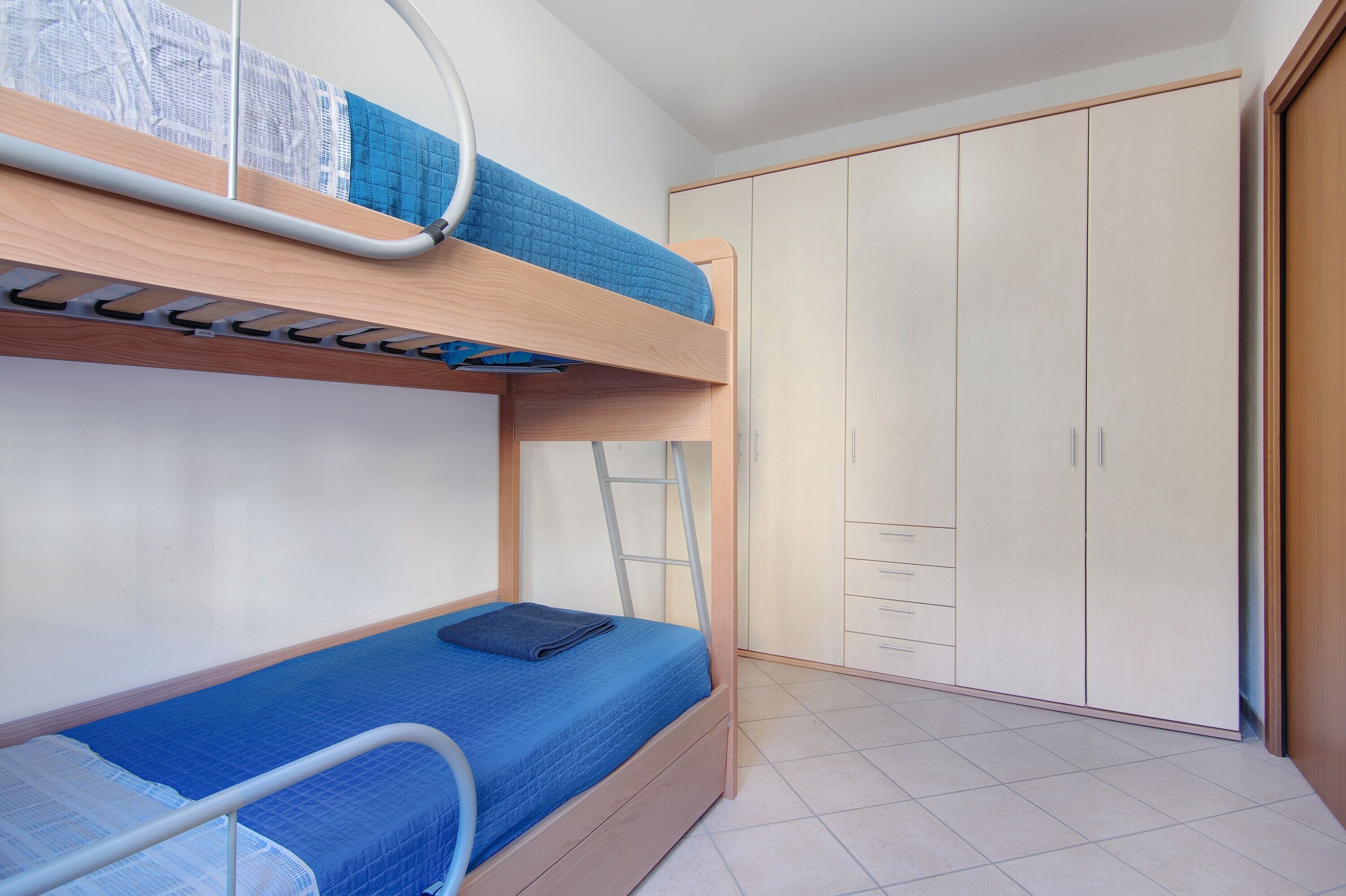 Un lit superposé avec une échelle, une armoire à plusieurs portes et un sol carrelé.