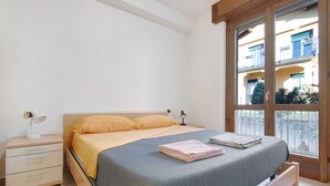 A bedroom with a bed, a nightstand, a lamp, and a window with a view of buildings. - Holiday Home "Casa Lierna" with Private Terrace, Balcony and Wi-Fi (Lierna)