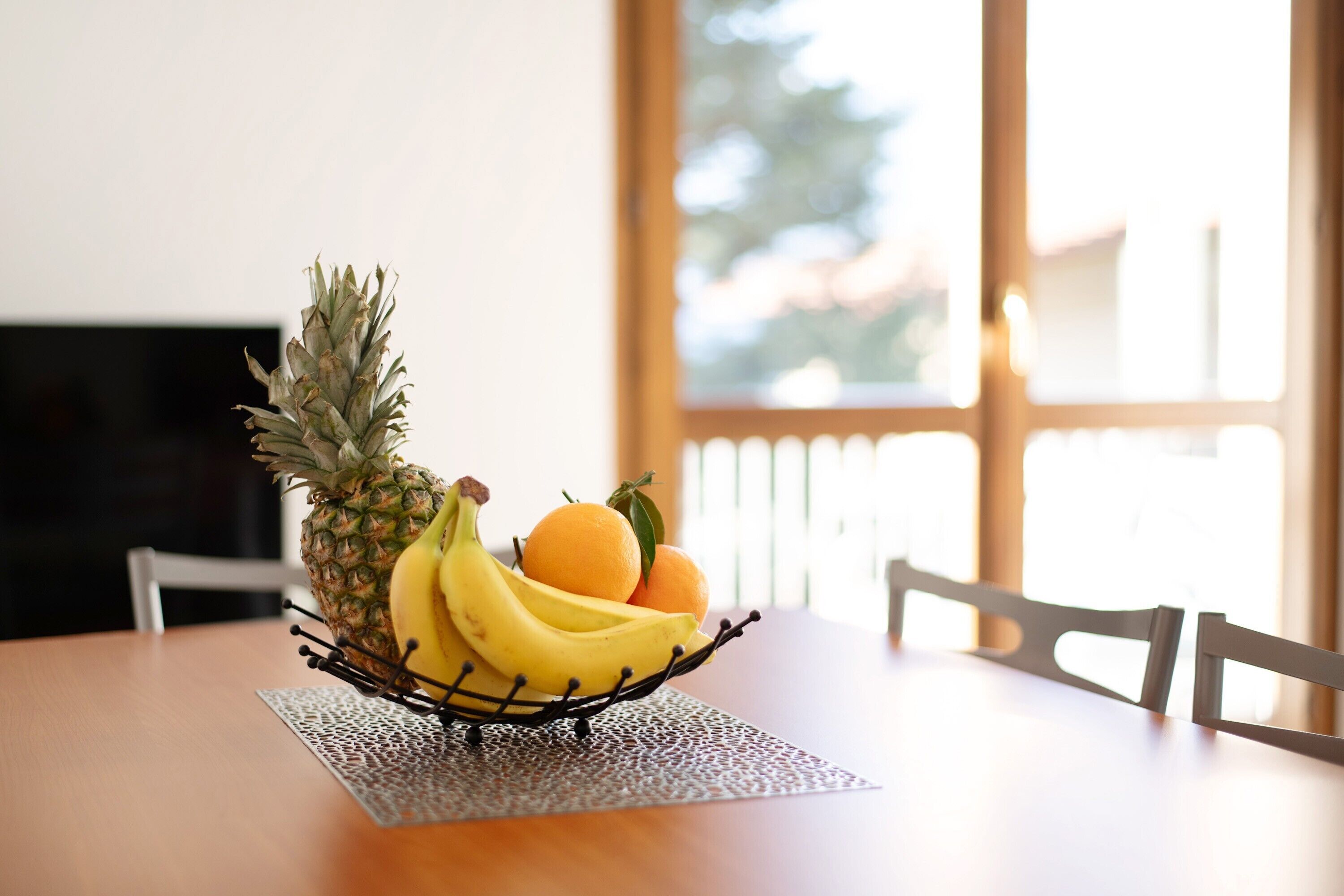 Ein Tisch mit einer Obstschale, gefüllt mit Ananas, Bananen und Orangen.