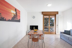 Un coin repas comprenant une table, des chaises, un panier de fruits, une horloge et un canapé.