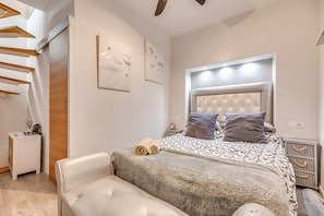 Une chambre à coucher moderne, comprenant un lit, un banc, une table de chevet et une tête de lit fixée au mur.