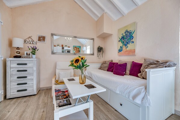 Une pièce chaleureuse avec un canapé blanc, une petite table sur laquelle est posé un vase, une commode, un miroir et un tableau accroché au mur.