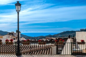 Une terrasse sur le toit, avec un lampadaire, des plantes en pot et une vue sur la mer et les collines.