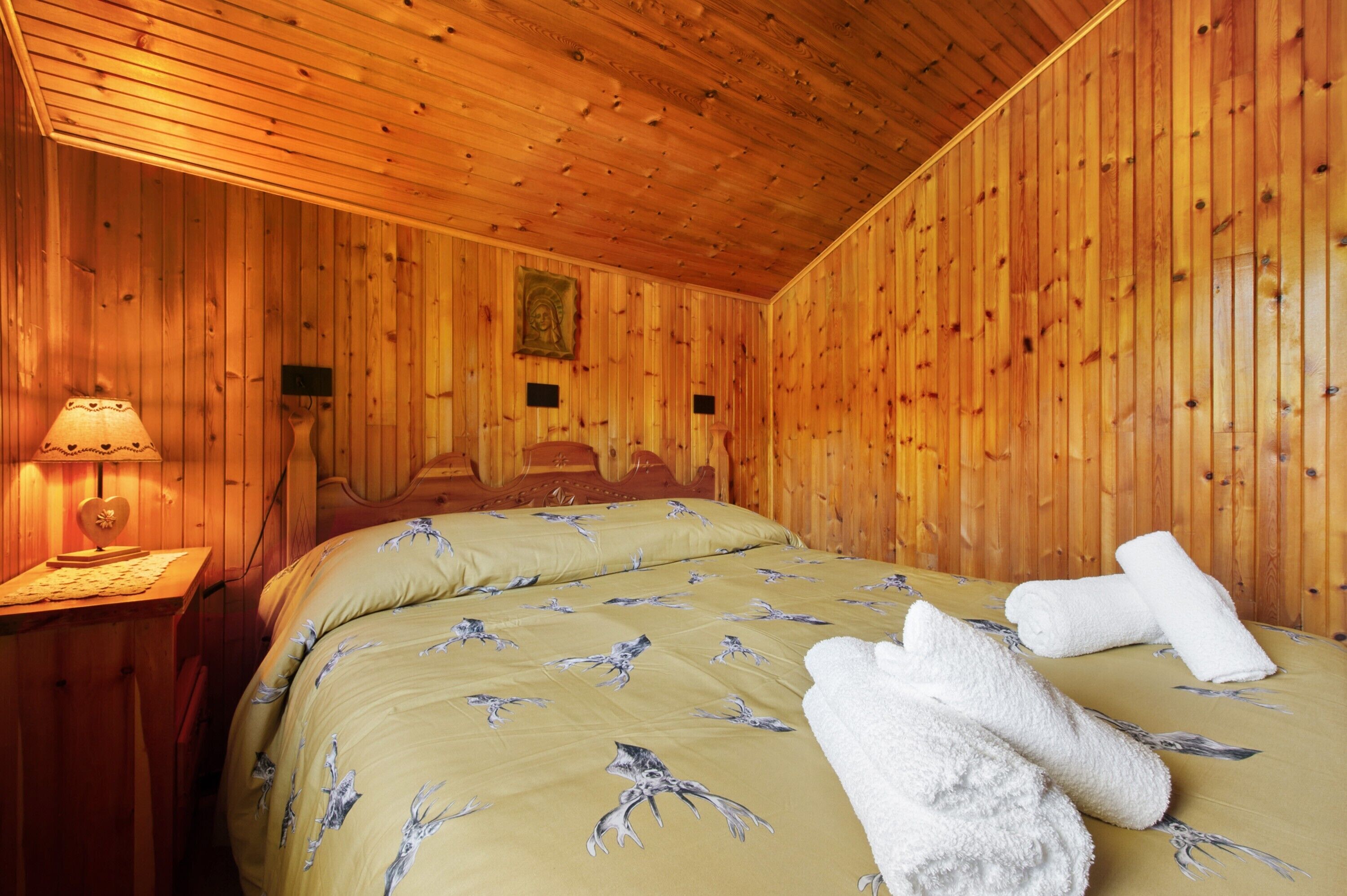 A wooden-paneled room with a bed, a nightstand, and a wall-mounted lamp.