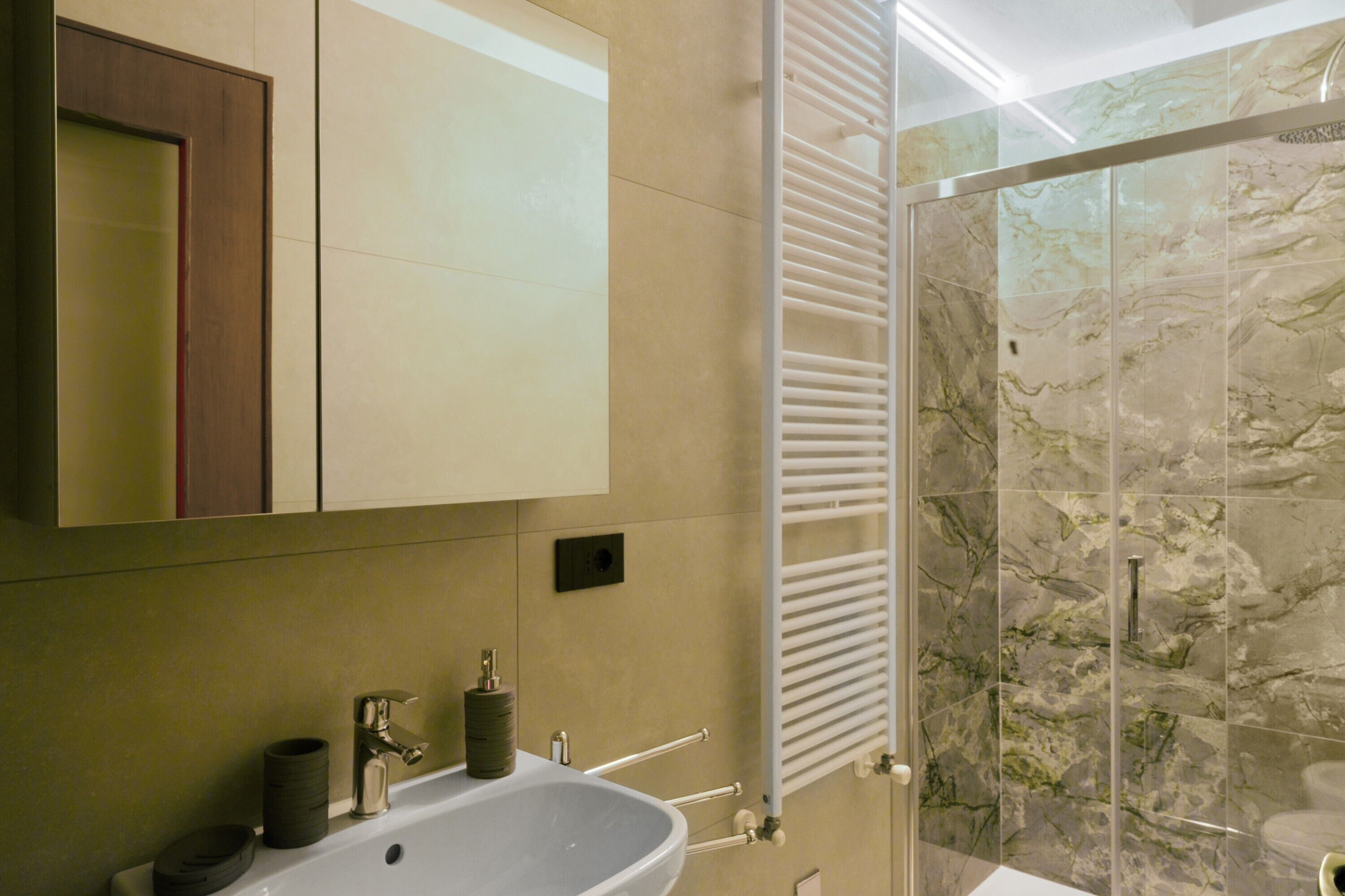 Une salle de bain équipée d’un lavabo, d’un miroir, d’un porte-serviettes et d’une cabine de douche en verre.