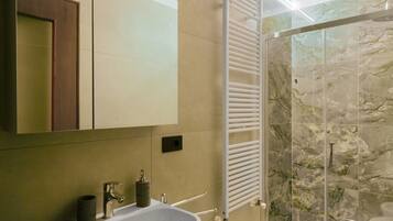 Une salle de bain équipée d’un lavabo, d’un miroir, d’un porte-serviettes et d’une cabine de douche en verre.