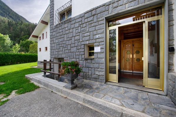 A stone building with a wooden door, a number 74 sign, and a potted plant with flowers.