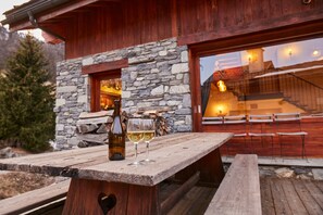 A wooden outdoor dining area with a stone wall and a bottle of wine.