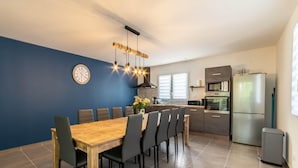 A modern kitchen with a dining area, featuring a wooden table, chairs, a clock, and a stainless steel refrigerator. - Villa 'Gite Les Bouches Rouges' with Mountain View, Wi-Fi and Air Conditioning (Vesseaux)