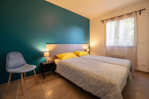 A bedroom with a bed, a chair, a nightstand, and a window with curtains.