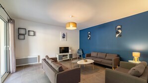 A modern living room with a blue accent wall, a flat-screen TV, a sofa, a coffee table, and a lamp. - Villa 'Gite Les Bouches Rouges' with Mountain View, Wi-Fi and Air Conditioning (Vesseaux)