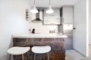 Una cucina con un piano di lavoro bianco, due lampade a sospensione, una parete decorata con pietra e un frigorifero in acciaio inossidabile.