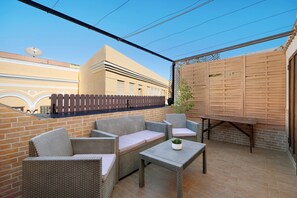 Un patio techado con muebles de mimbre, pared de ladrillo y valla de madera.