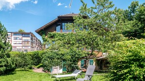 Ein Gebäude mit Balkon, ein Garten mit Rasen und Bäumen sowie zwei Liegestühlen.