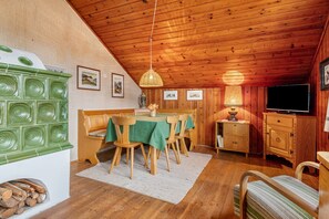 A wooden interior with a dining table, chairs, a television, and a fireplace.