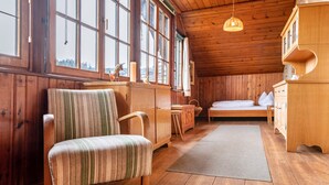Ein Holzhütten-Interieur mit einem Bett, einem Holzschrank, einem gestreiften Sessel und großen Fenstern.