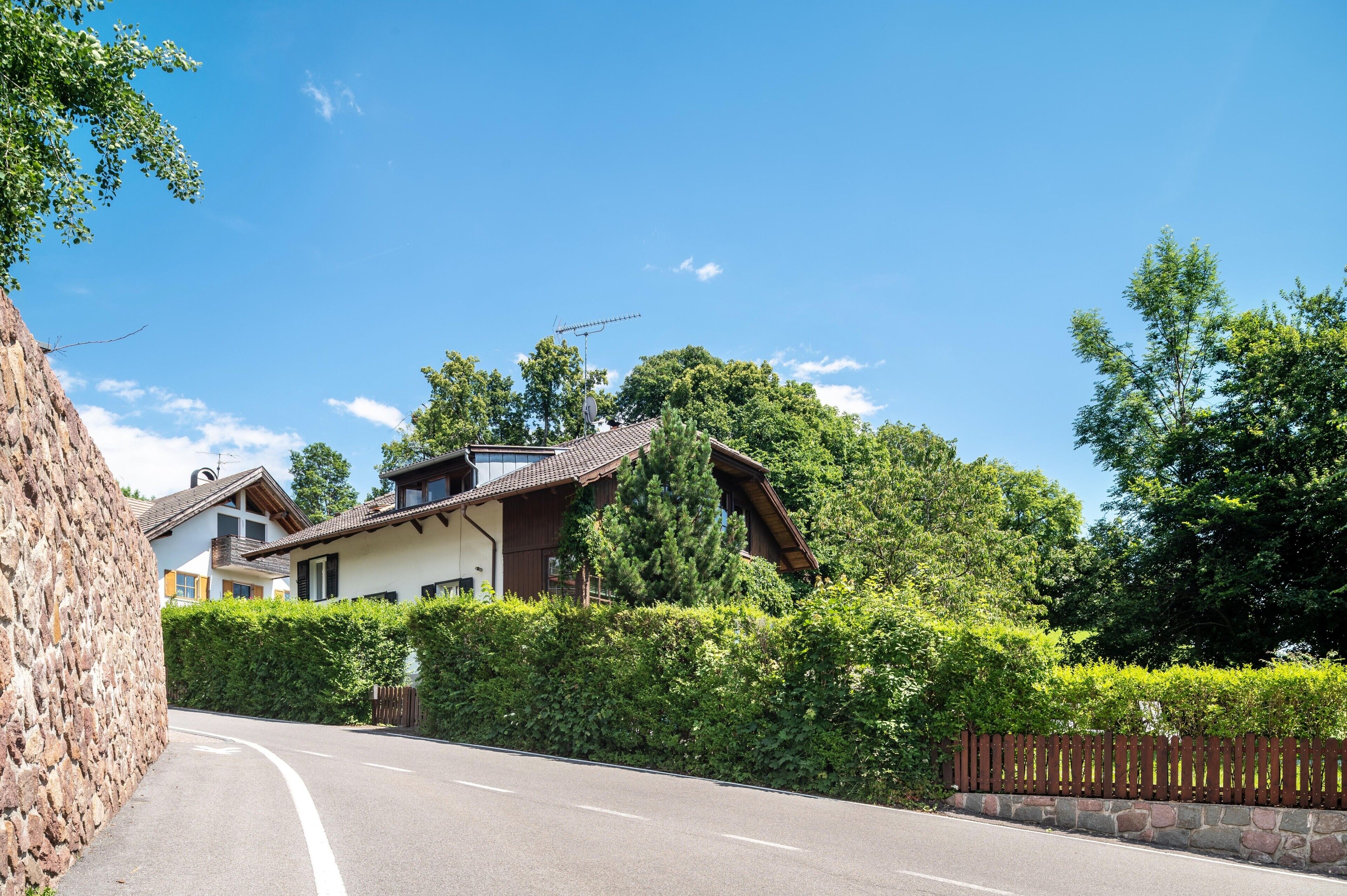 A residential area with a curved road, stone wall, and houses with sloped roofs.