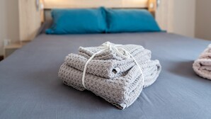 Ein ordentlich bezogenes Bett mit einer grauen Decke und einem gefalteten Handtuch.