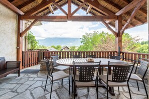 Un espace extérieur aménagé, abrité et doté d’un sol en pierre, de tables et de chaises en bois, et offrant une vue sur les montagnes.