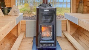 A Harvia wood stove in a wooden cabin with a view of trees and a lake.