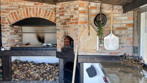 A brick fireplace with a wooden mantel, a pizza oven, and a fire pit area with logs.