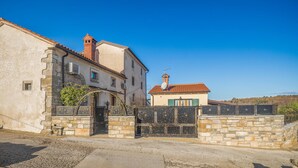 A traditional stone building with a tiled roof, a gated entrance, and a clear blue sky.