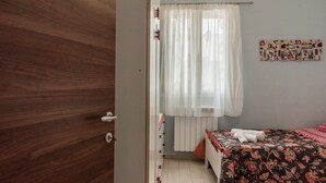 Una camera da letto con una porta in legno, un letto con copripiumino floreale, una tenda bianca e un condizionatore d'aria a parete.