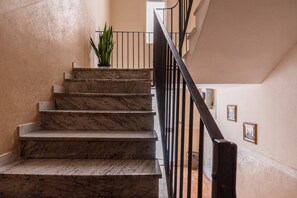 Un escalier en marbre avec une rampe noire, une plante en pot et des tableaux encadrés accrochés au mur.