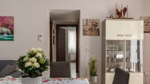 Un'area pranzo con un tavolo apparecchiato per due, un vaso di fiori, un mobile con vetrine e un quadro appeso al muro.