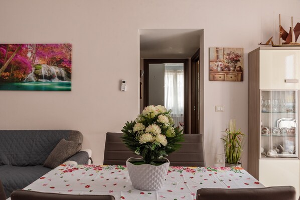 Un coin repas avec une table dressée pour deux personnes, un canapé, un buffet contenant de la verrerie et un tableau représentant une cascade.