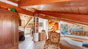 Ein gemütliches Dachzimmer mit Holzbalken, einem floralen Sessel, einer Couch und einer kleinen Küchenzeile.