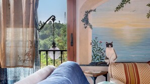 Ein Zimmer mit Blick auf Grünflächen, ein Landschaftsgemälde und eine Katze auf einer Bank.