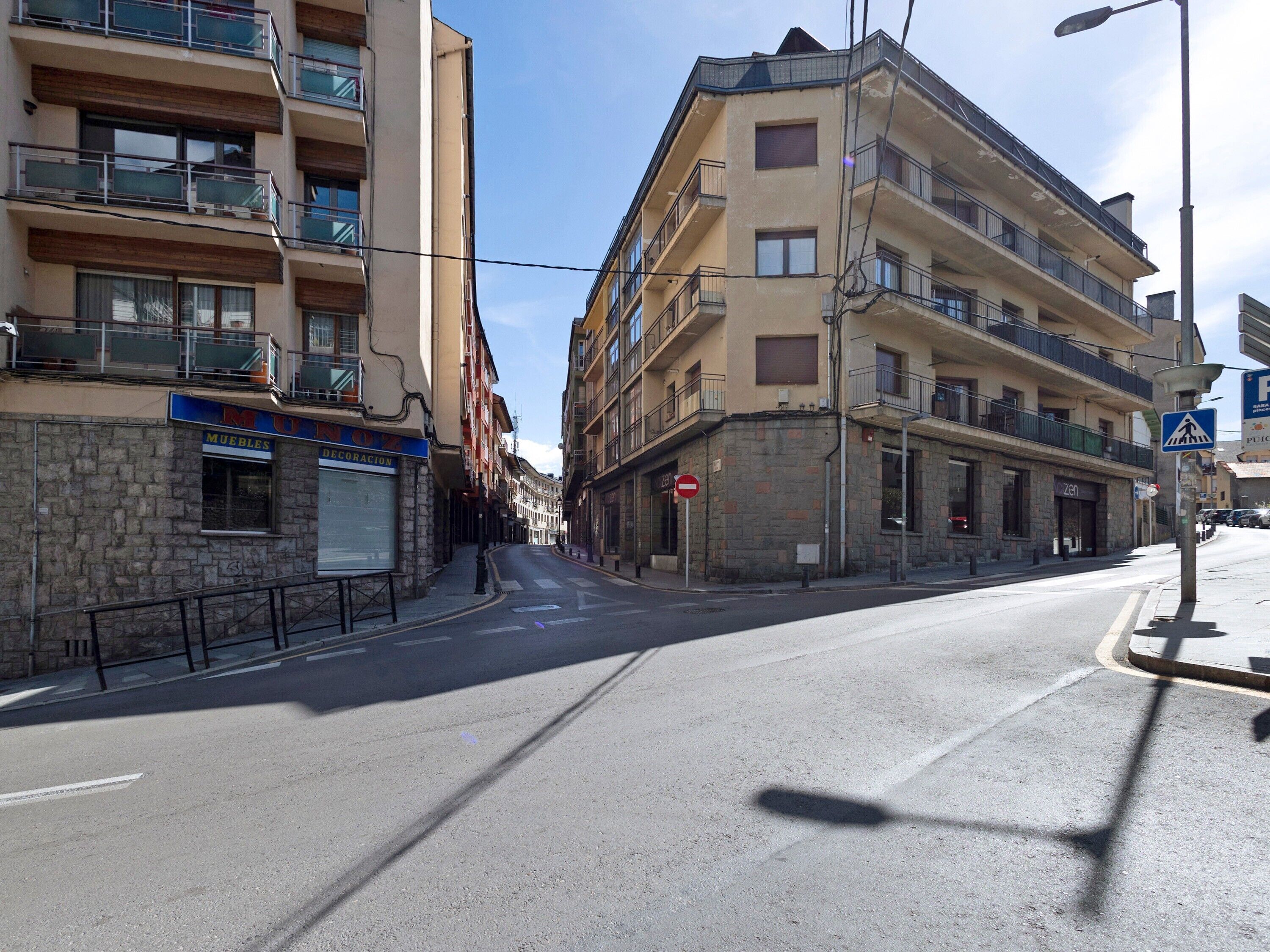 A street with multi-story buildings, a closed storefront, and a pedestrian crossing sign.