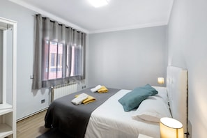 A bedroom with a bed, a bedside lamp, a window with curtains, and a radiator.