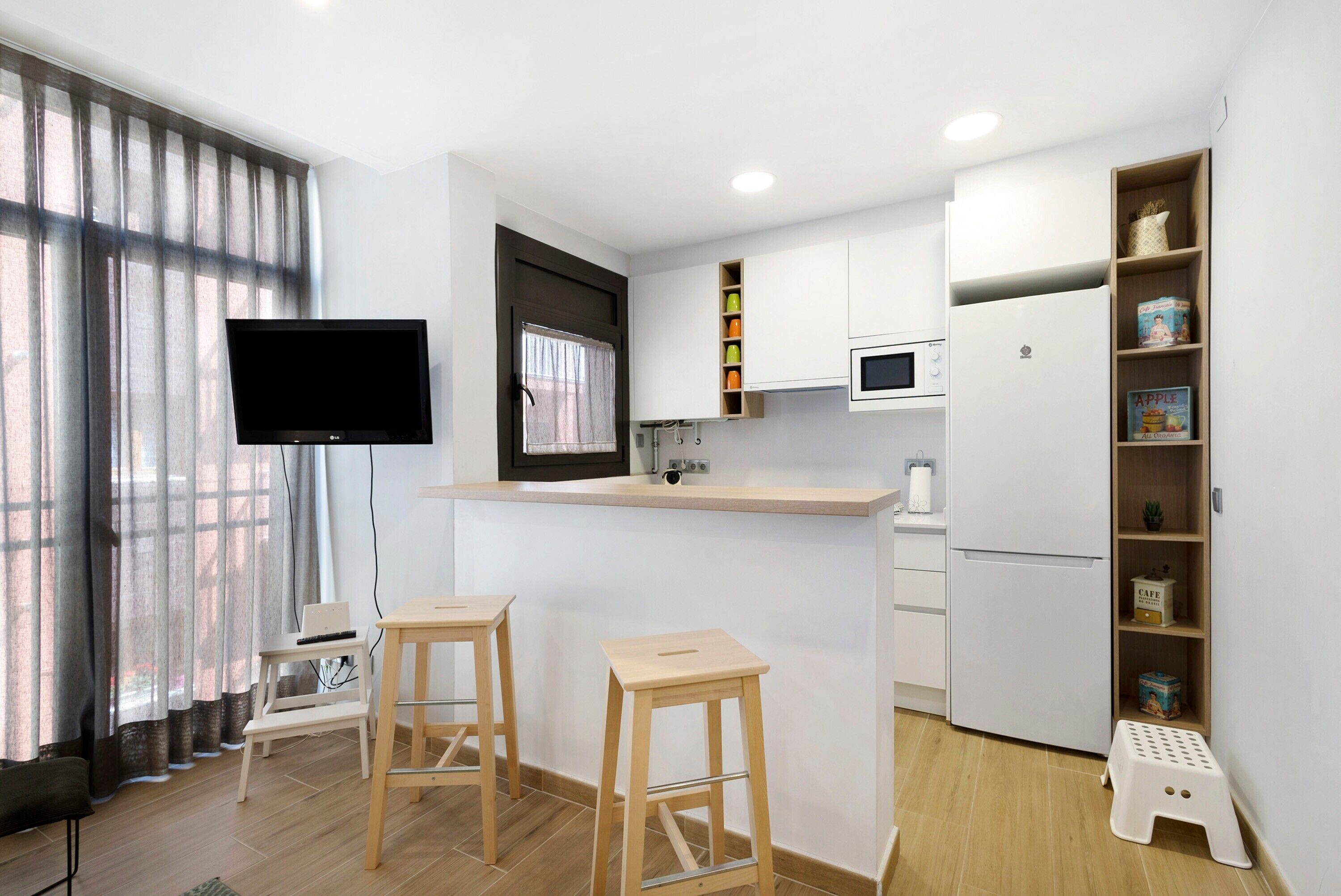 Eine moderne Küche mit Flachbildfernseher, Holzbarhocker, Mikrowelle und Kühlschrank.