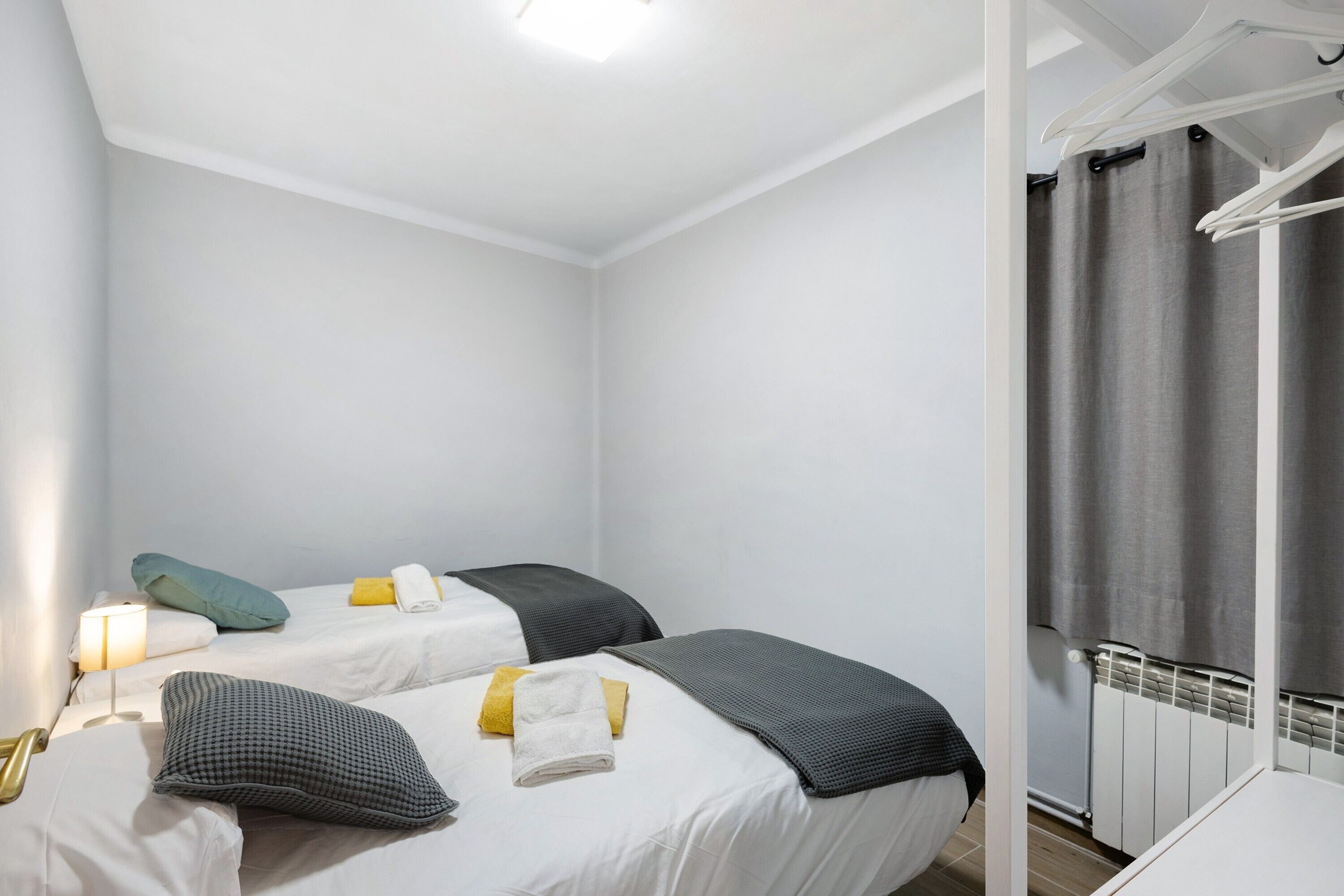 Une chambre avec deux lits, chacun équipé d’un oreiller et d’une couverture, une table de chevet avec une lampe et une fenêtre avec des rideaux.