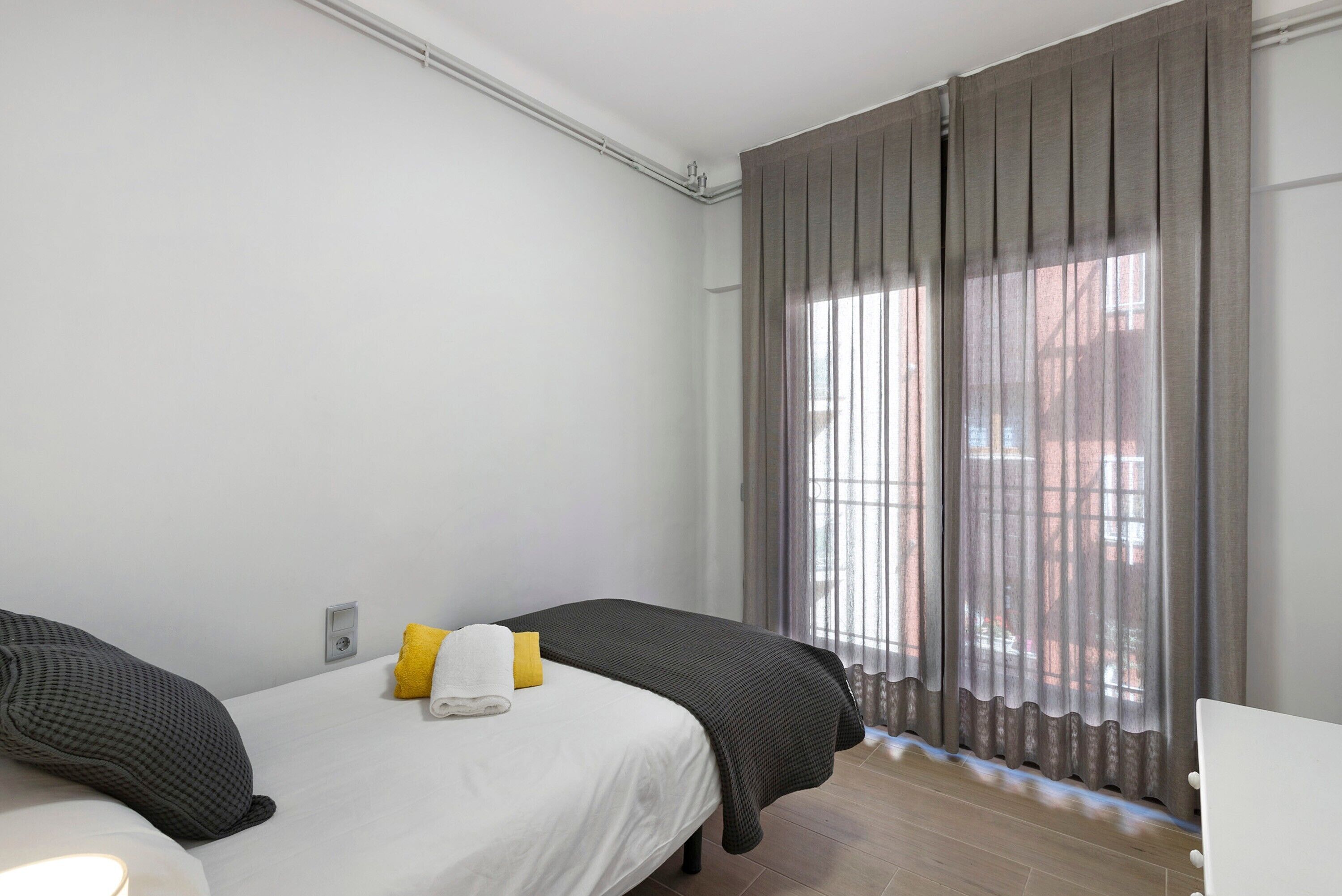 A bedroom with two beds, a window with curtains, and a visible wall socket.