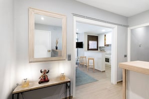 A modern interior with a large mirror, a small table with decorative items, and a view into a kitchen area.
