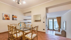 Un coin repas avec une table en verre et des chaises en bois, une cuisine à l’arrière-plan et un balcon avec un canapé.
