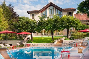 Una piscina amb gandules i ombrelles, una casa amb grans finestres i un jardí ben cuidat.