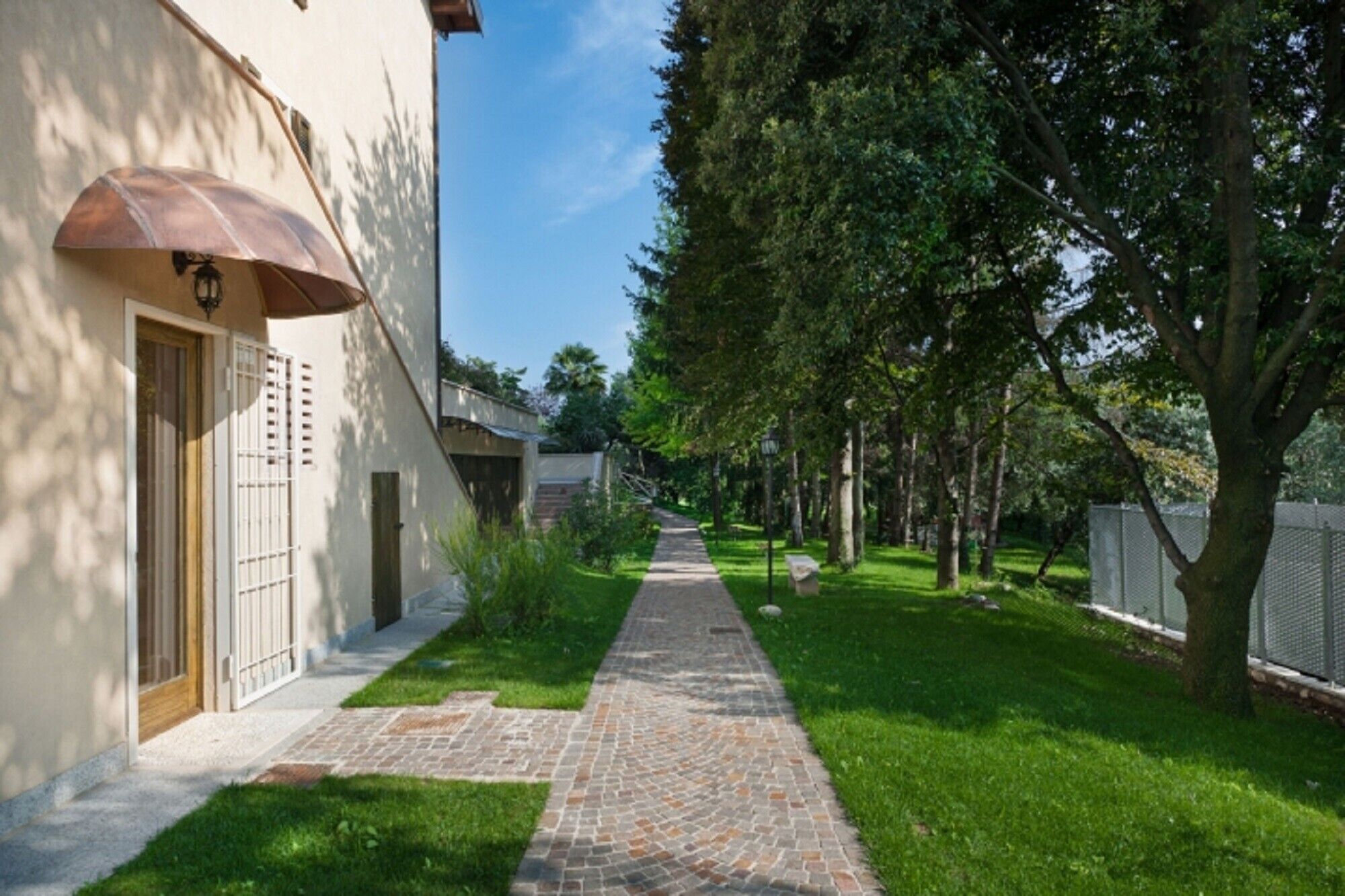 Un chemin menant à un bâtiment doté d’une porte et d’une fenêtre, entouré de verdure et d’arbres.