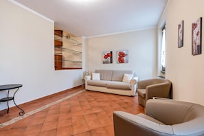 Un salon comprenant un canapé, des fauteuils, une petite table et une étagère en verre.