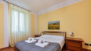 A hotel room with a bed, two bedside tables, a painting on the wall, and a window with curtains. - Oleadei - Eolo Apartment with Mountain View, Wi-Fi, and Air Conditioning (San Felice del Benaco)