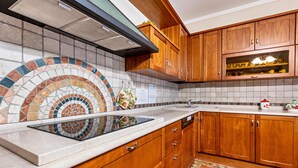 A kitchen with wooden cabinets, a tiled backsplash, a built-in oven, and a sink. - Oleadei - Eolo Apartment with Mountain View, Wi-Fi, and Air Conditioning (San Felice del Benaco)