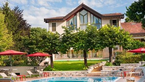 Ein Pool mit Liegestühlen und Sonnenschirmen, ein Haus mit großen Fenstern und ein gepflegter Rasen.